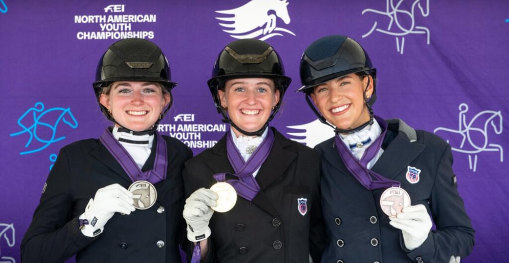 Three young ladies holding up medals.