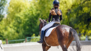 A girl with pigtails riding in a dressage arena.