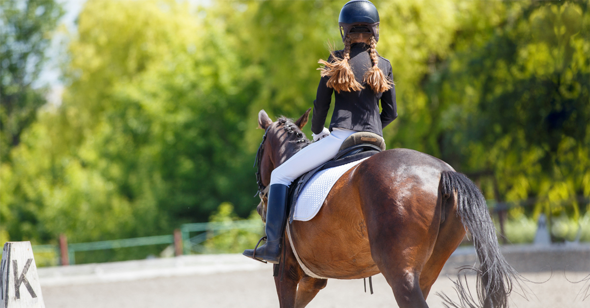 A girl with pigtails riding in a dressage arena.