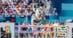 A man jumping a grey horse over a fence at the Olympics.