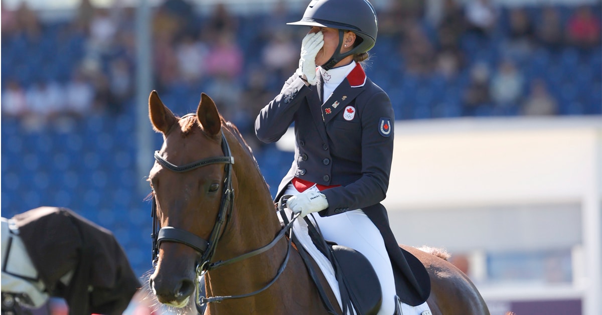 A woman on a dressage horse holding her hand to her face in amazement.