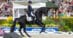A woman performing a dressage test on a black horse.