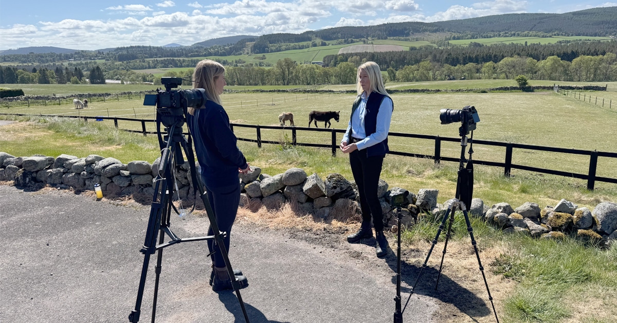 Two women standing beside a field having a discussion on camera.
