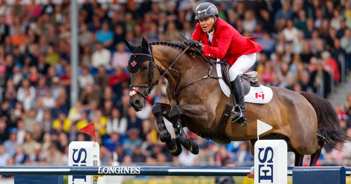 A man wearing a red jacket jumping a bay horse over a fence in Aachen.