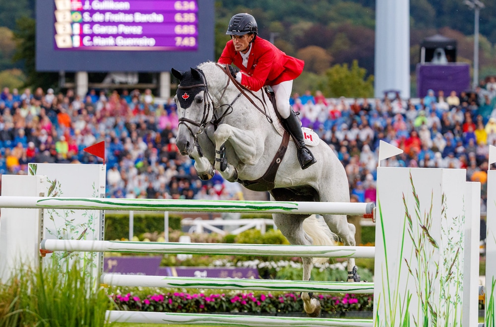 A man wearing a red jacket jumping a horse over a fence in Aachen.