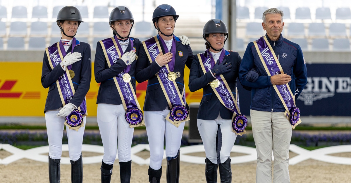 A team of para riders on a podium with hands over hearts.
