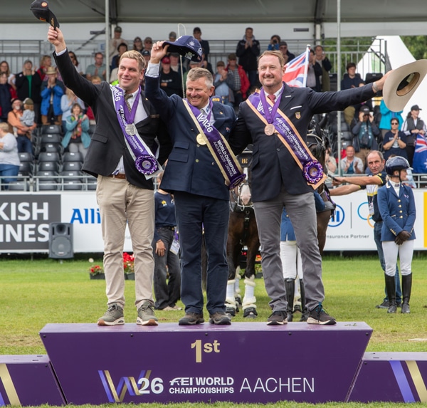 Three men standing, waving, on a podium.