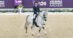 A woman riding a grey dressage horse in competition.