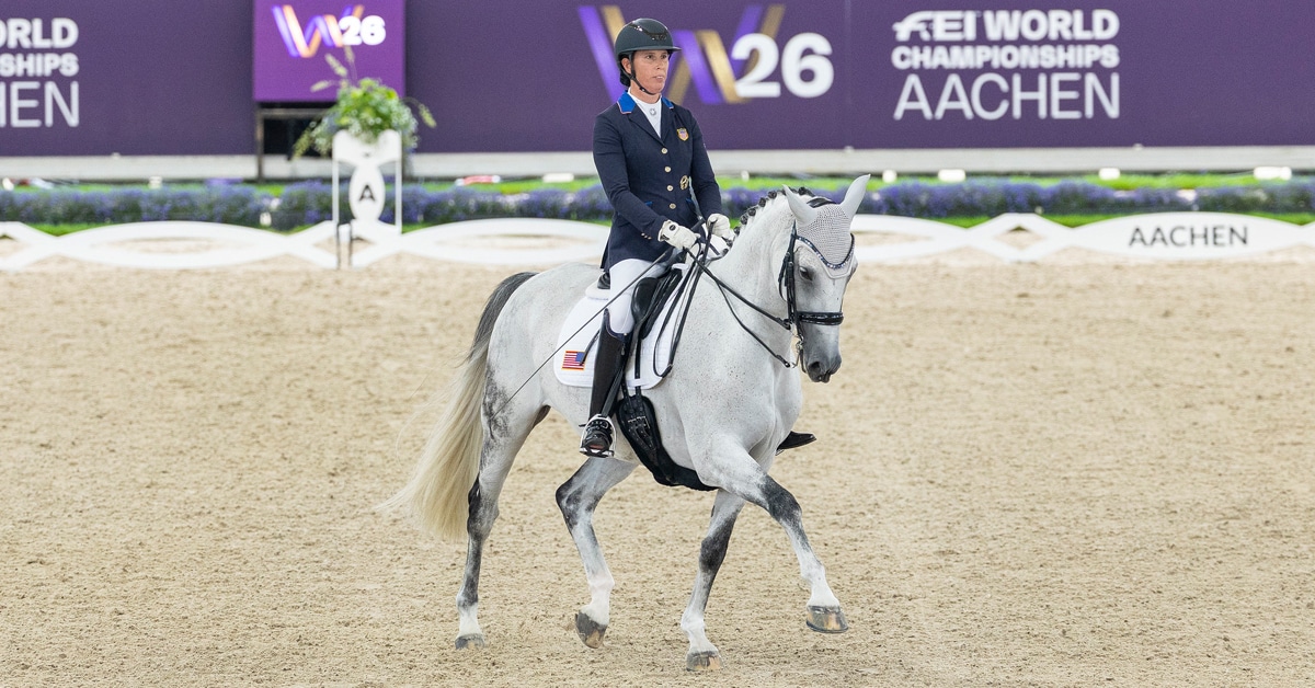 A woman riding a grey dressage horse in competition.