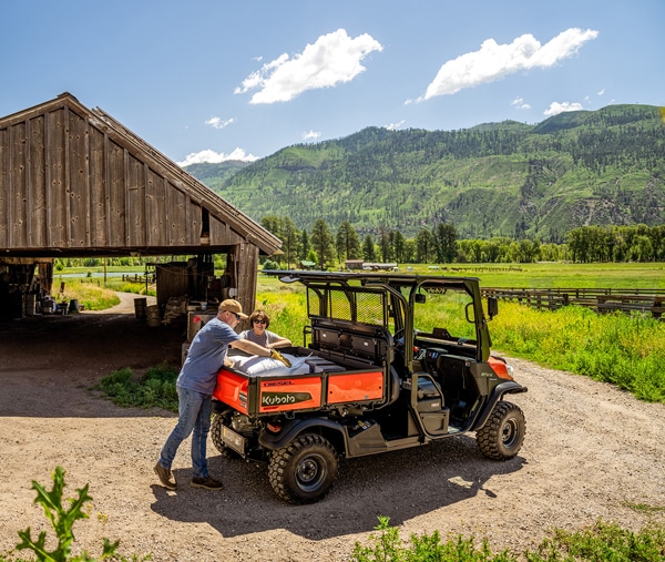 A couple loading supplies into a utility vehicle on a farm.