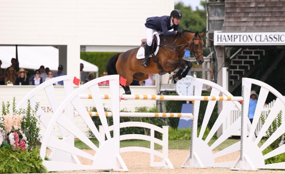 A man jumping a bay horse over a fence in the Hamptons.