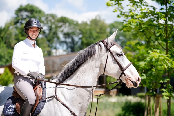 A smiling woman sitting on a grey horse.