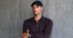 A man wearing a Rolex watch and a baseball cap posing against a grey wall.