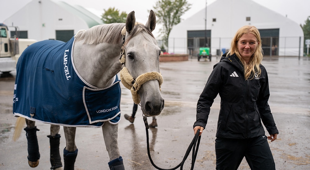 A woman leading a grey horse.