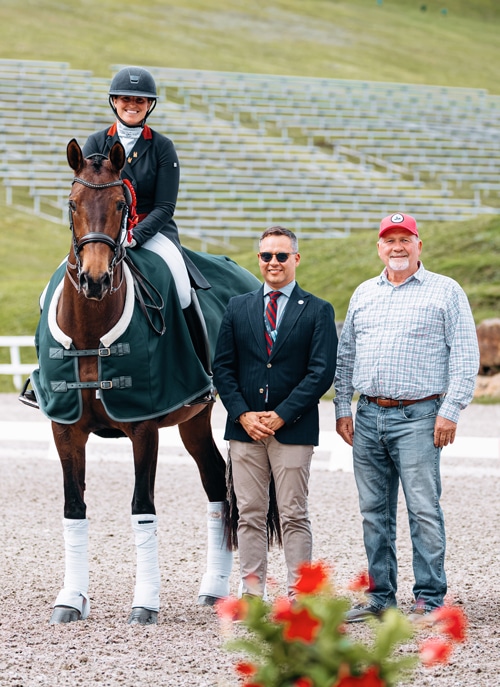 A woman on a bay horse with two men during a presentation.