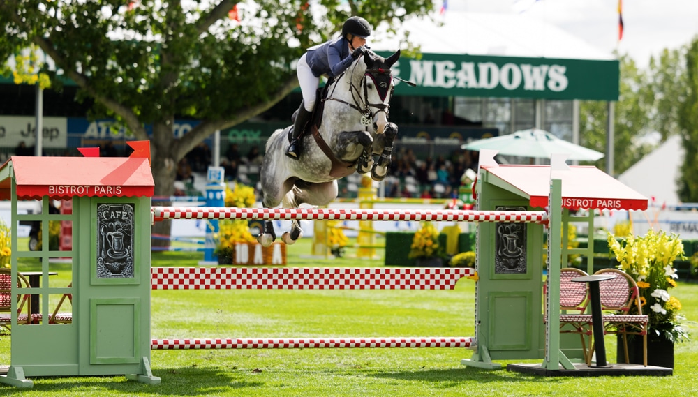 A woman jumping a grey horse over a fence at Spruce Meadows.