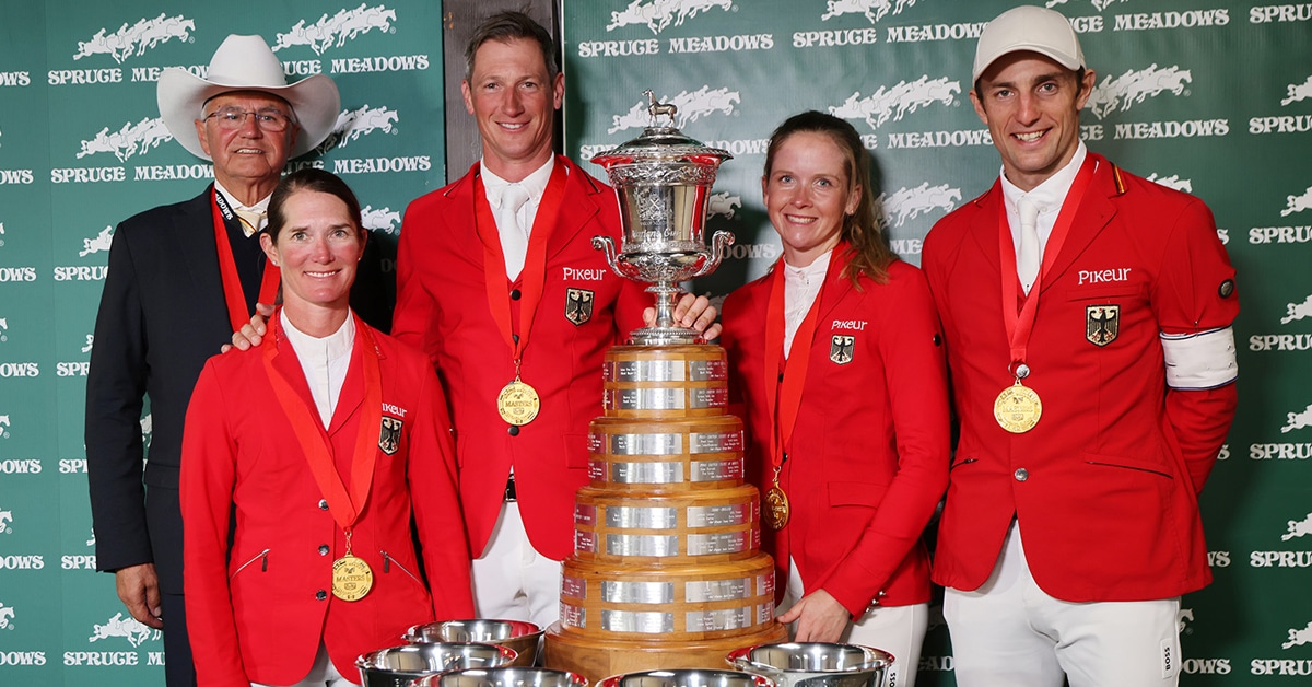 A team wearing red jackets standing with a large trophy.