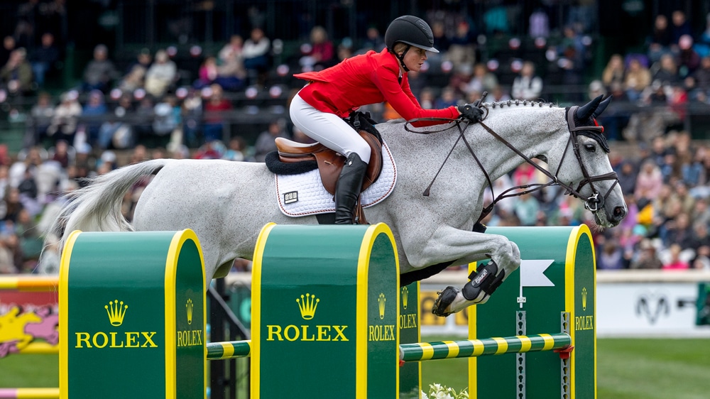 A woman jumping a grey horse over a fence at Spruce Meadows.