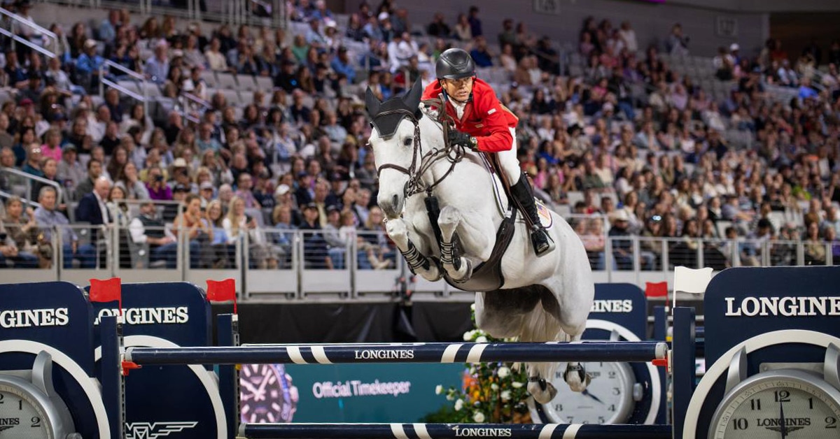 A man jumping a grey mare over a fence at a horse show.