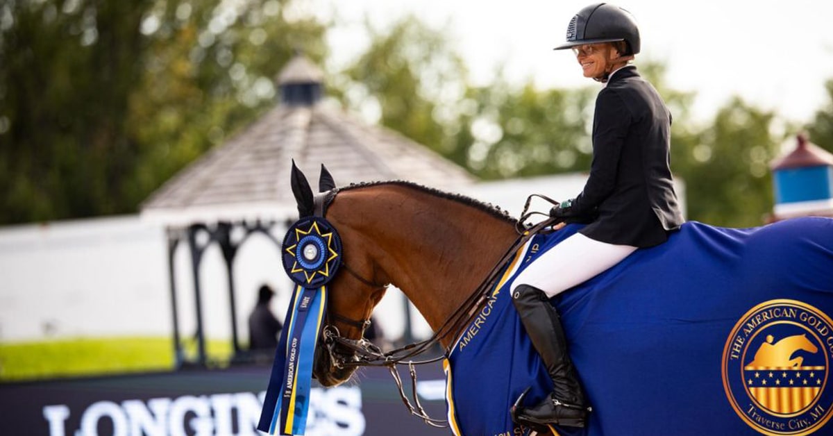 A smiling woman on a bay horse during a prize ceremony.