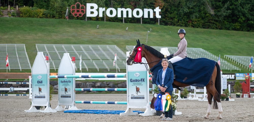 A smiling woman on a bay horse during a presentation.
