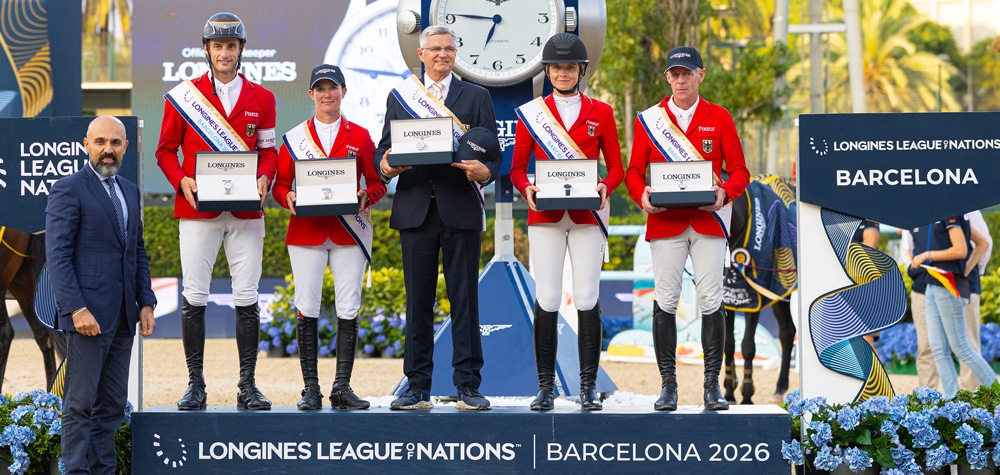 A group of riders in red jackets and watches standing on a podium.