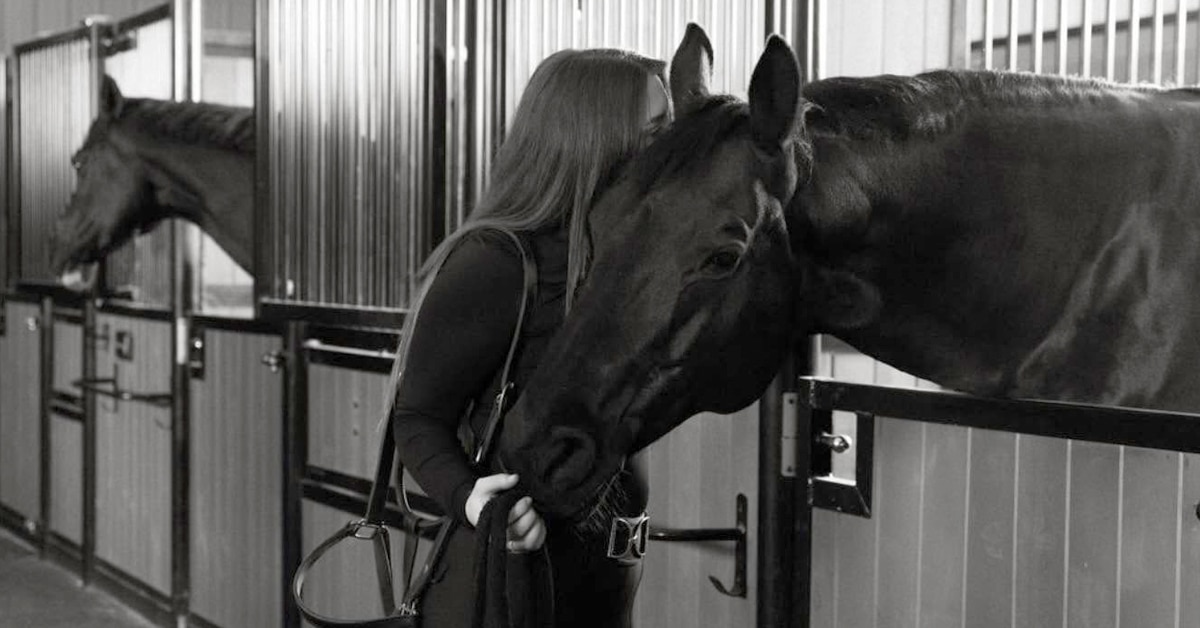 A black-and-white photo of a woman hugging a horse in a barn.