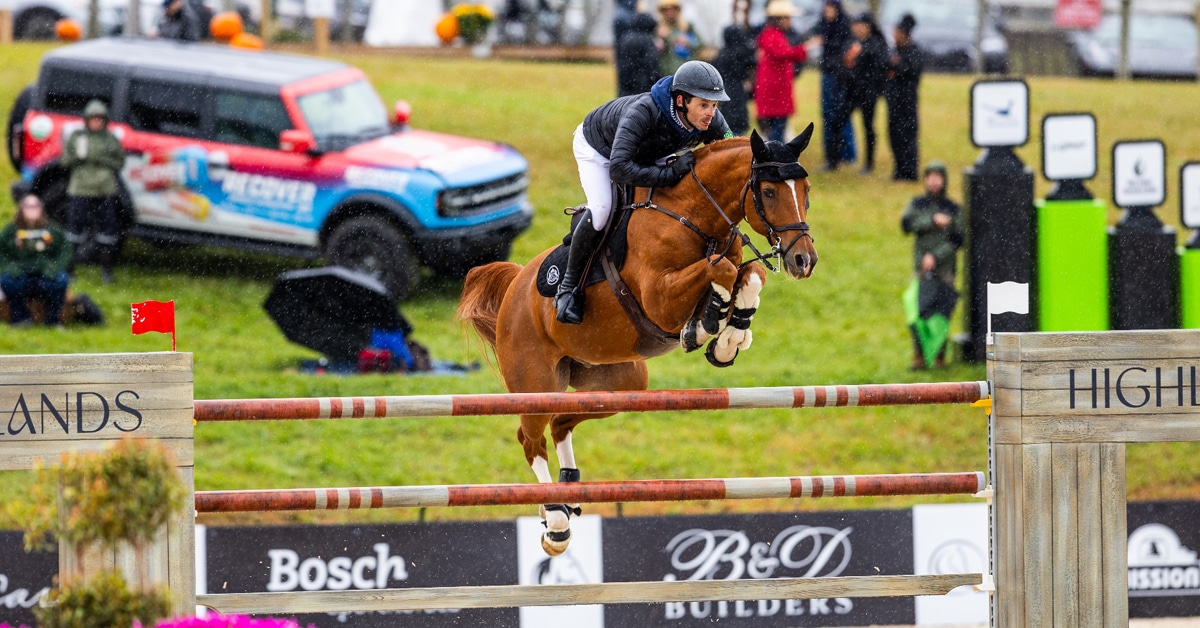 A man jumping a chestnut horse over a fence in the rain.