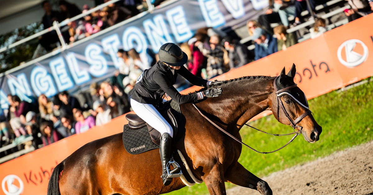 A woman patting her horse while walking out of the ring.