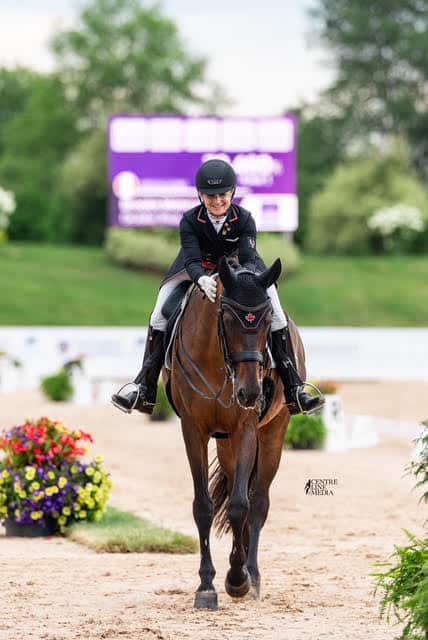 A woman patting her bay dressage horse on the way out of the arena.