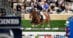 A woman jumping a bay horse over a fence in an indoor arena.