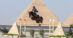 A man jumping a bay horse over a fence in Cairo with a pyramid in the background.